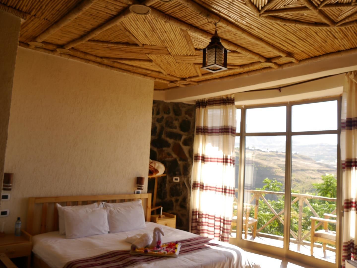 A bedroom with a large bed, a stone wall, and a view of the outdoors.
