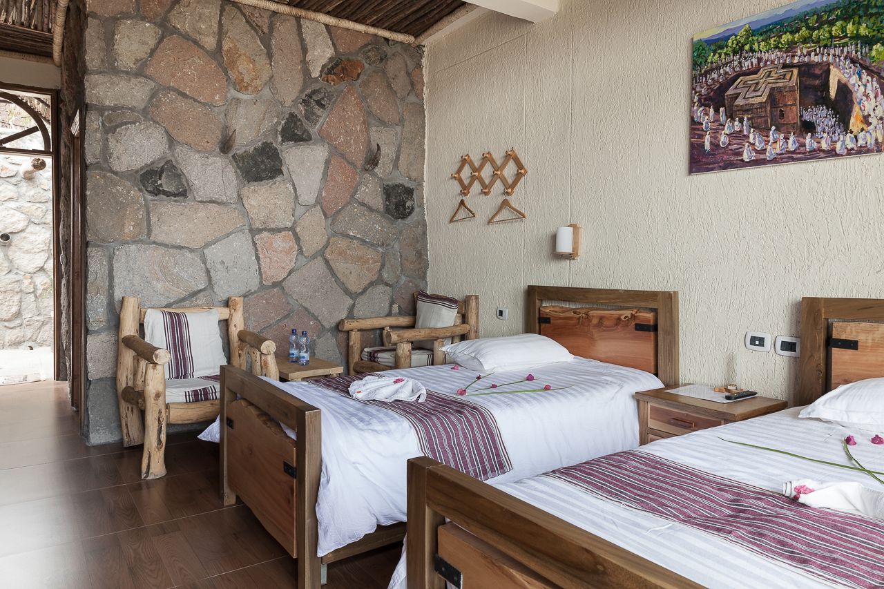 A room with stone walls, wooden beds, and a painting of a historical scene.