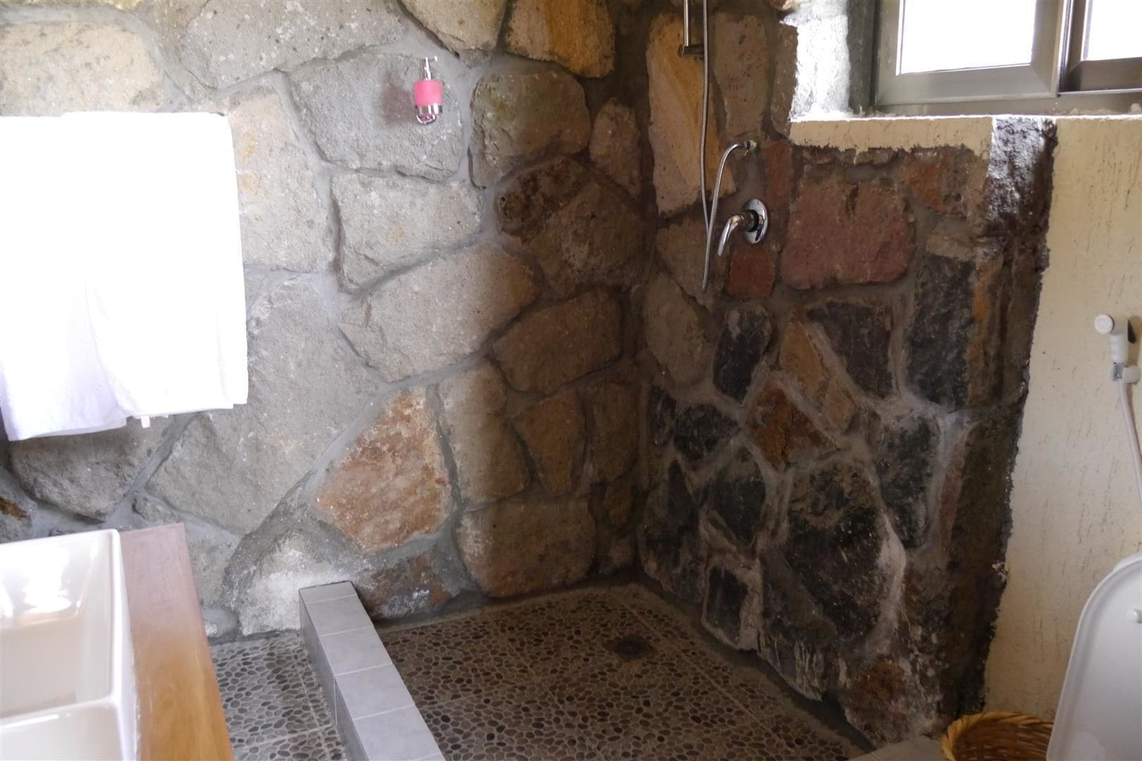 Un baño de paredes de piedra con ducha, una toalla colgada en la pared y suelo de baldosas.