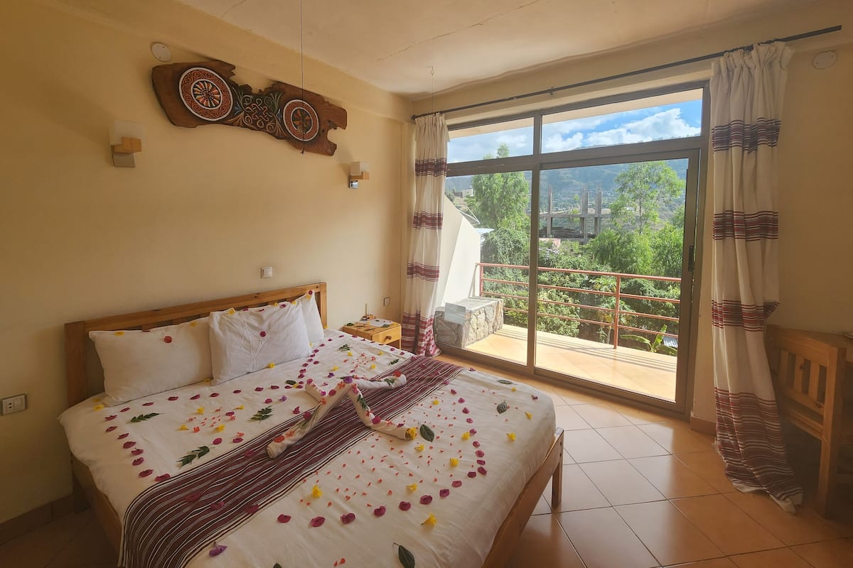 Une chambre avec un grand lit, une vue sur la verdure grâce à une porte coulissante, et un élément décoratif mural.