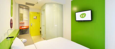 A hotel room with a bed, a green accent wall, a TV, and a bathroom with a yellow door.