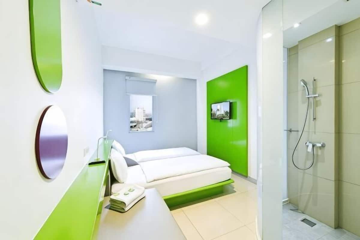 Una habitación de hotel moderna con cama, ducha, pared de acento verde y televisor montado.