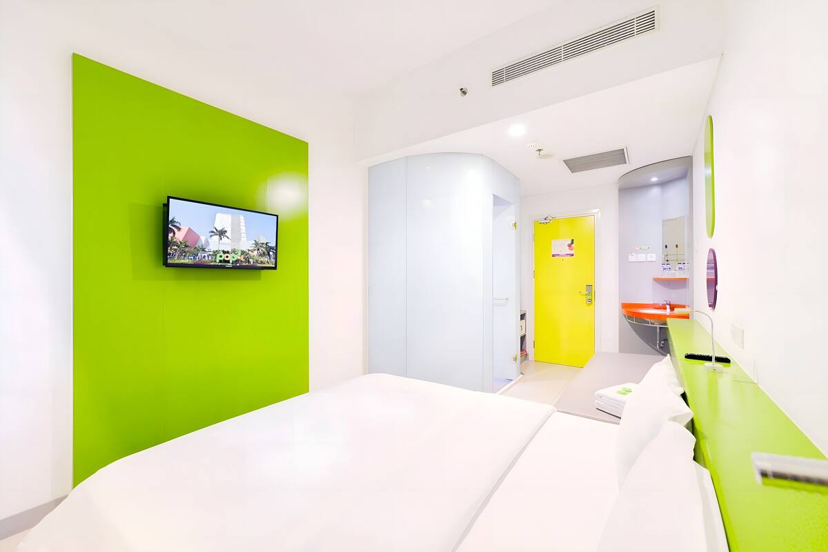 Una habitación de hotel moderna con una cama grande, un televisor montado en una pared verde y un baño con puerta amarilla.