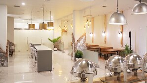 Un moderno hall de hotel con un bar central, zonas de estar y una escalera que lleva a los pisos superiores.