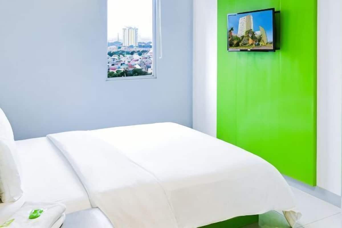 A hotel room with a bed, a window, and a green wall.