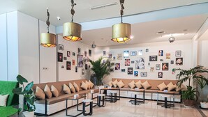 Un vestíbulo moderno con un sofá modular, varias mesas y una pared decorada con diversas fotografías enmarcadas.