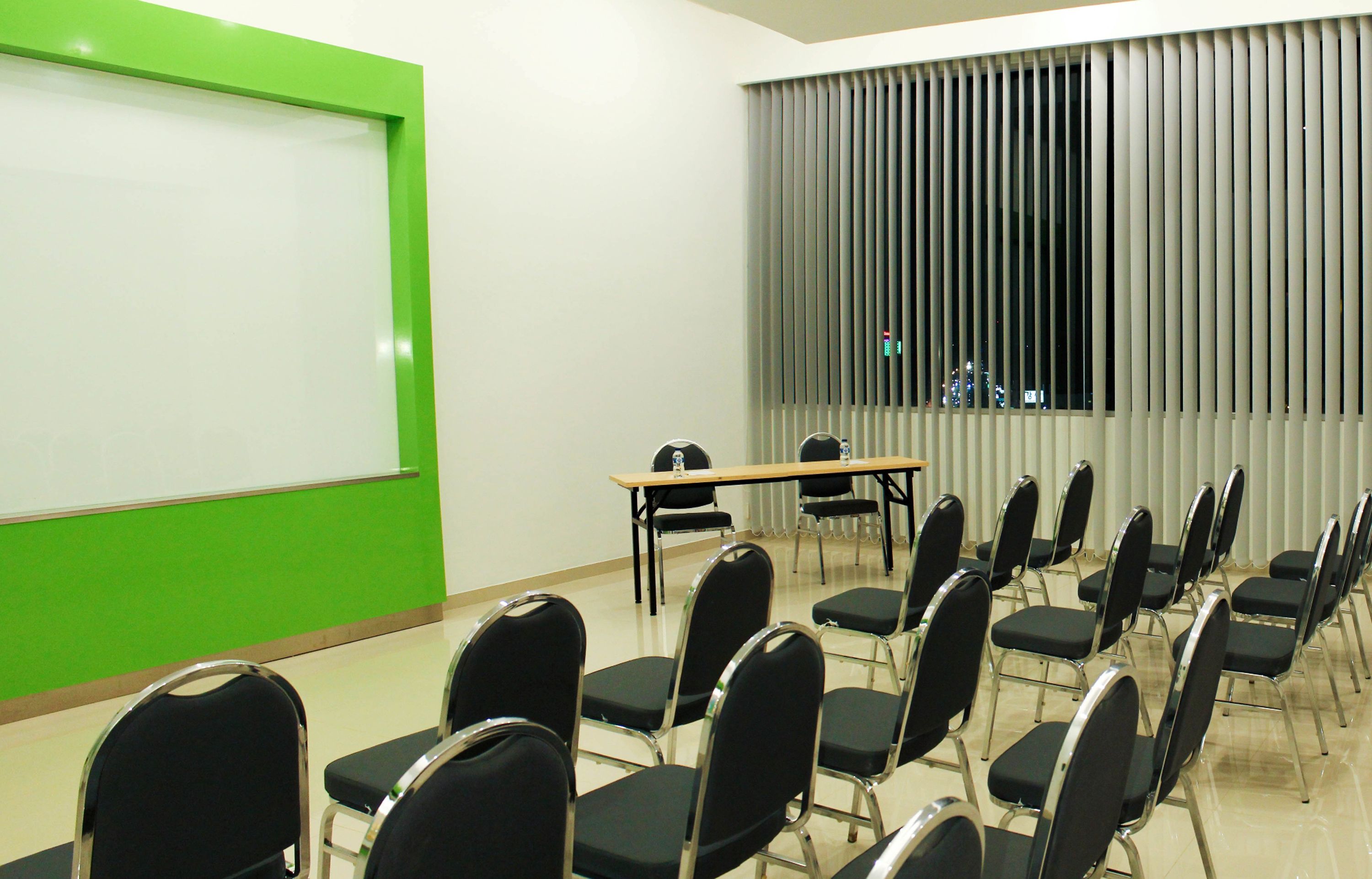 A conference room with a whiteboard, a projector screen, a table, and rows of chairs.