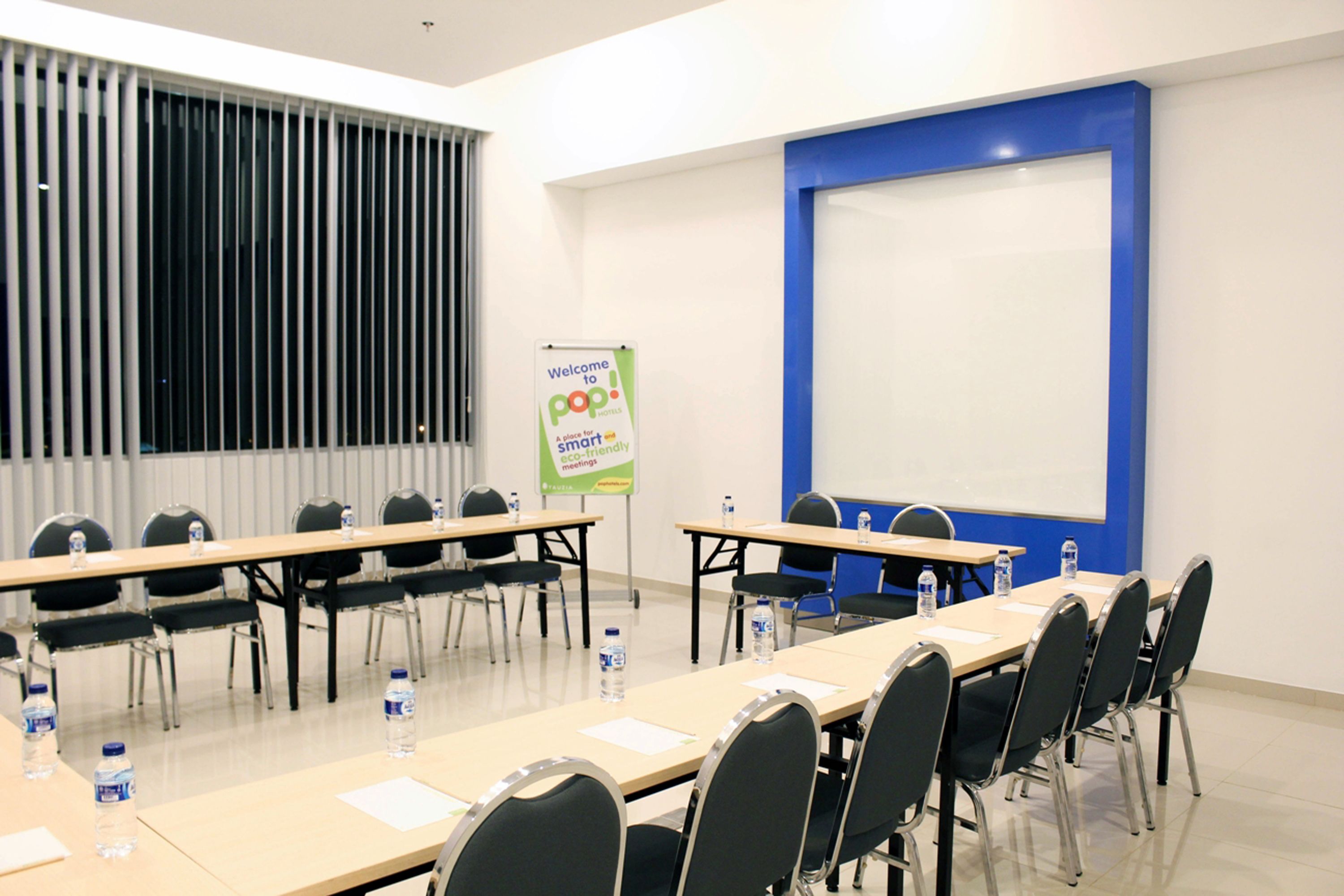 A conference room with a long table, chairs, water bottles, and a presentation screen.