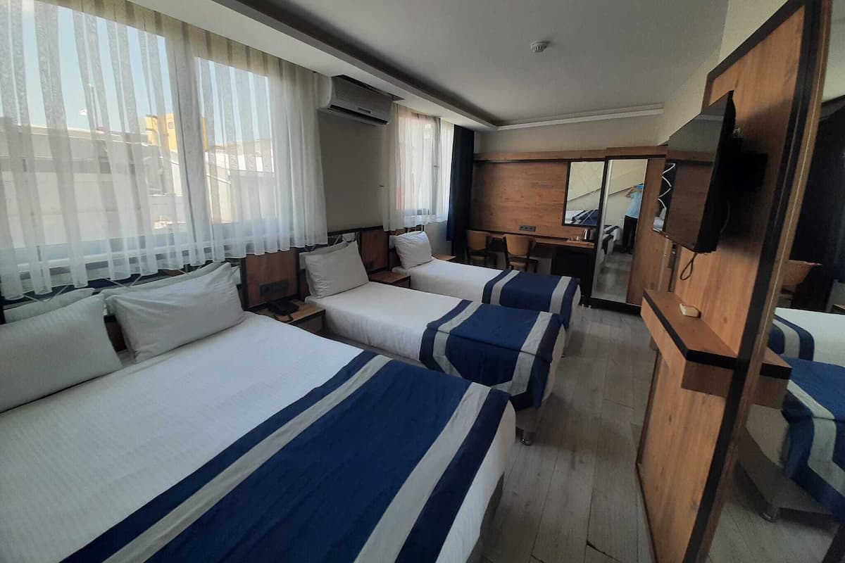 Une chambre d’hôtel avec deux lits, un bureau, une chaise, une télévision et une grande fenêtre avec des rideaux.