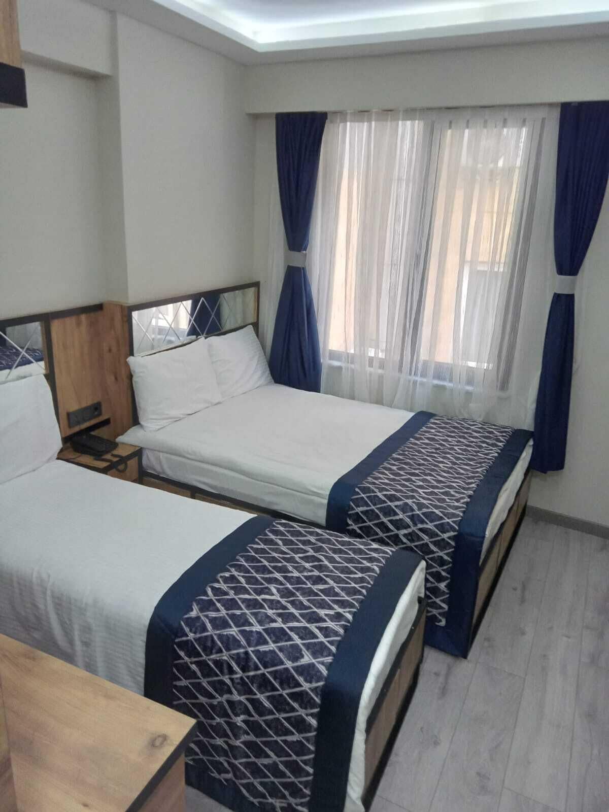 A bedroom with two beds, a wooden headboard, a nightstand, and a window with sheer curtains.
