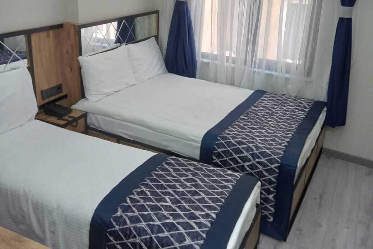 Une chambre avec deux lits, une tête de lit en bois, une table de chevet et une fenêtre avec des rideaux légers.