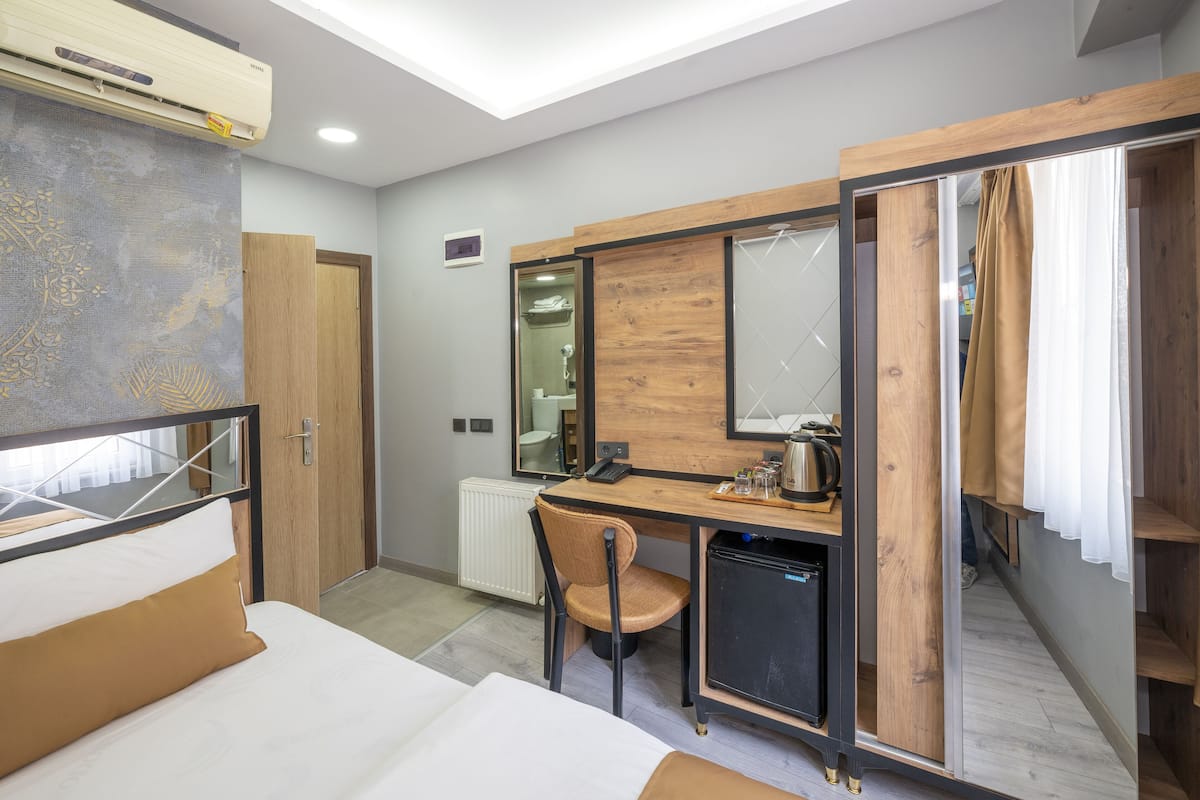 Une chambre d’hôtel comprenant un lit, un bureau avec une chaise, une petite kitchenette, un miroir et une armoire.