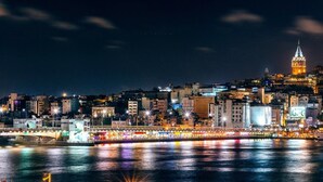 Paesaggio urbano notturno con una torre imponente, una passeggiata lungomare e edifici illuminati.