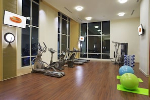 Ein Fitnessraum mit Trainingsgeräten, großen Fenstern und Holzboden.