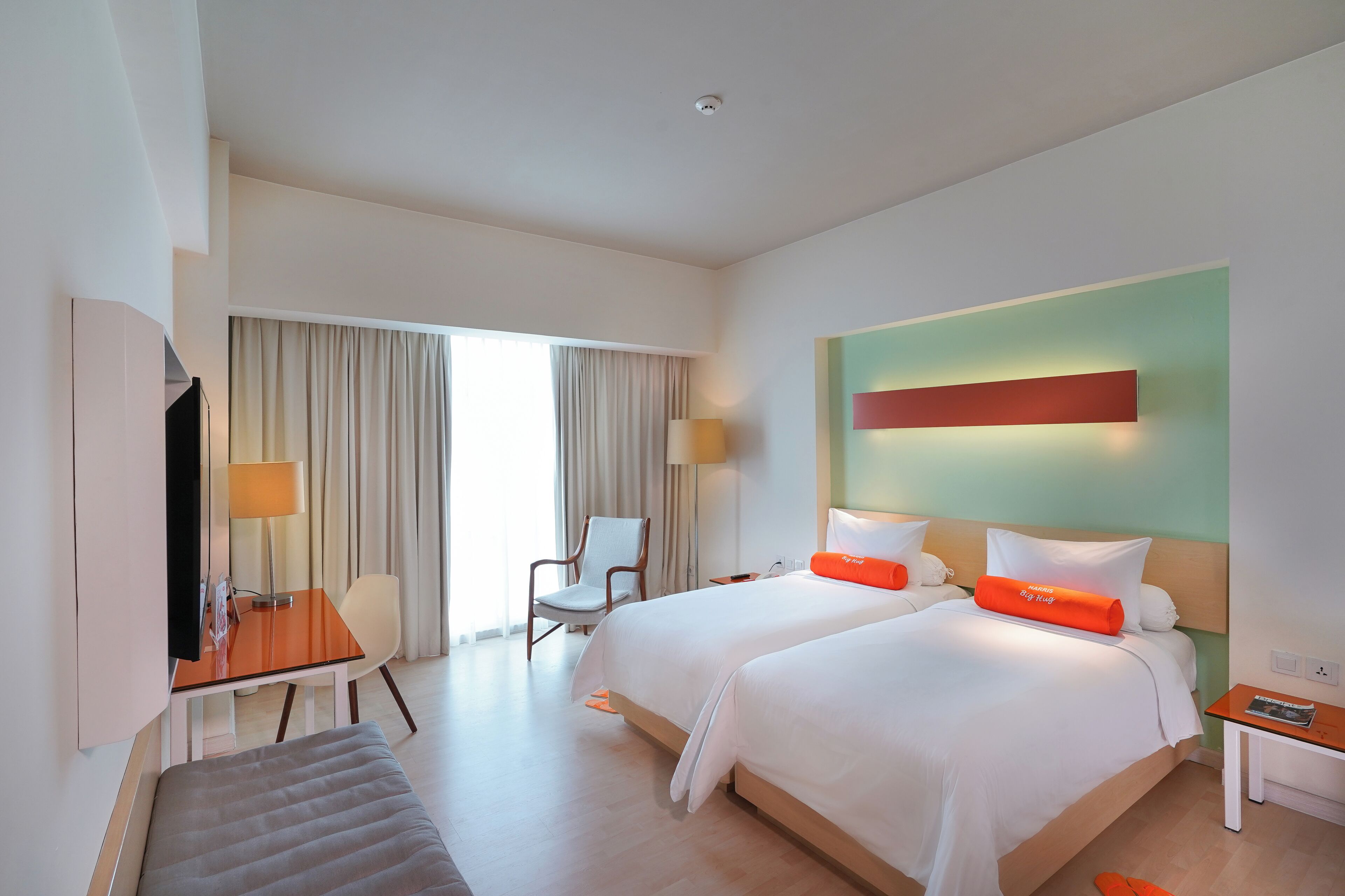 Quarto de hotel com duas camas, uma escrivaninha, uma cadeira e uma televisão.