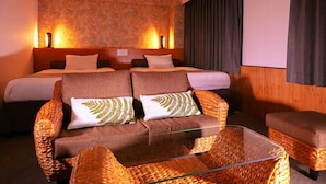 Une chambre d’hôtel avec un grand lit, deux canapés, une table basse en verre et un écran de projection.