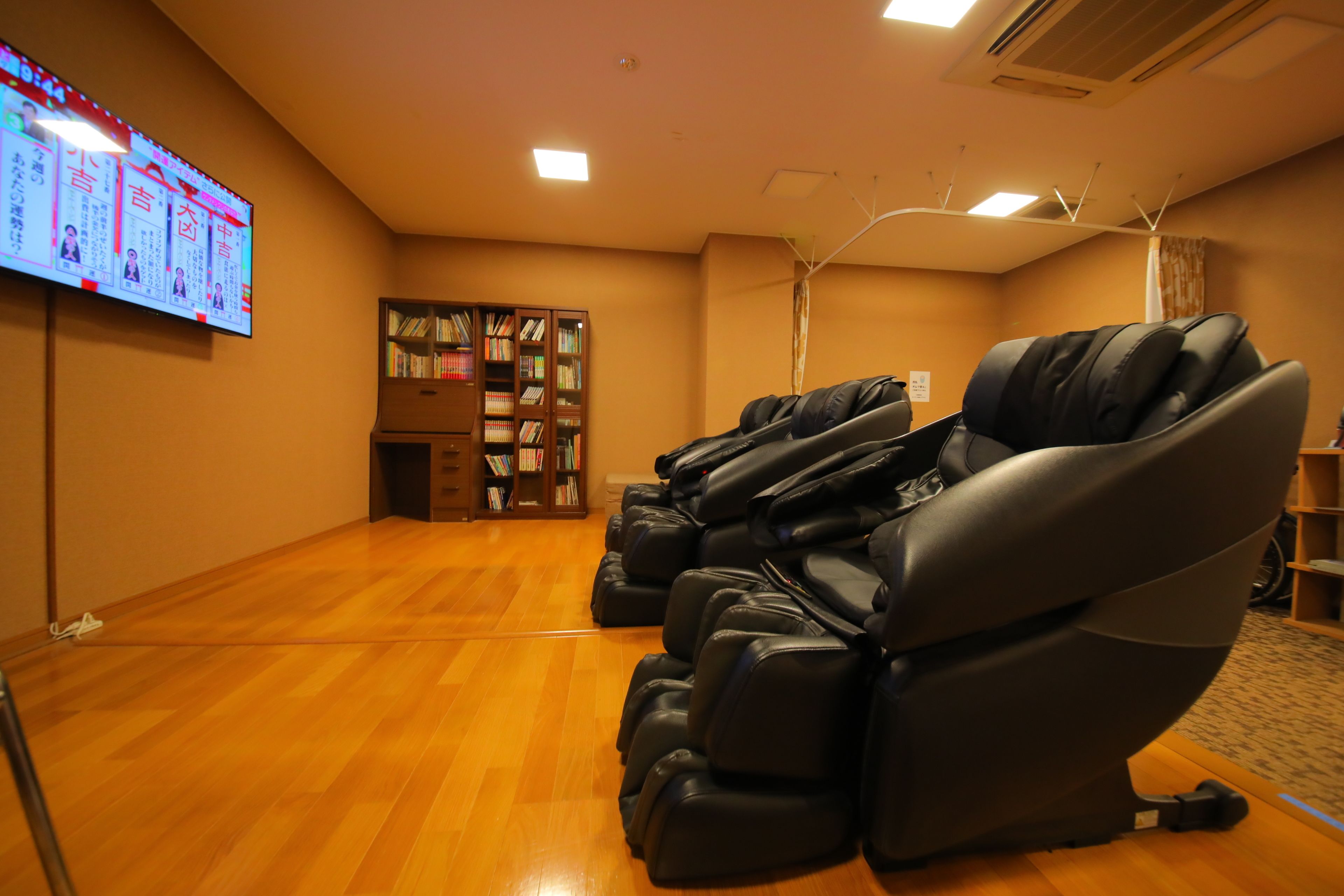 A room with massage chairs, a bookshelf, and a large screen displaying information.