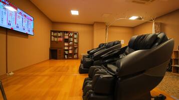 A room with massage chairs, a bookshelf, and a large screen displaying information.