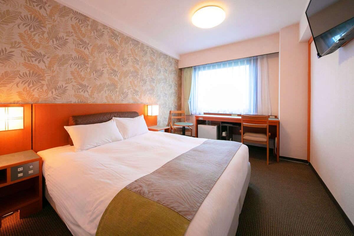 Een hotelkamer met een groot bed, een bureau, een stoel, een televisie en een raam met gordijnen.