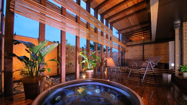 Un espace dédié à un bain à remous, doté d’un sol en bois, de paravents en bambou et de plantes en pot.