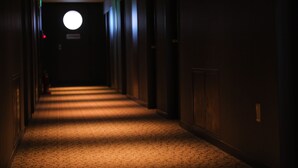 Un couloir faiblement éclairé, doté d’un sol recouvert de moquette et de murs en bois.