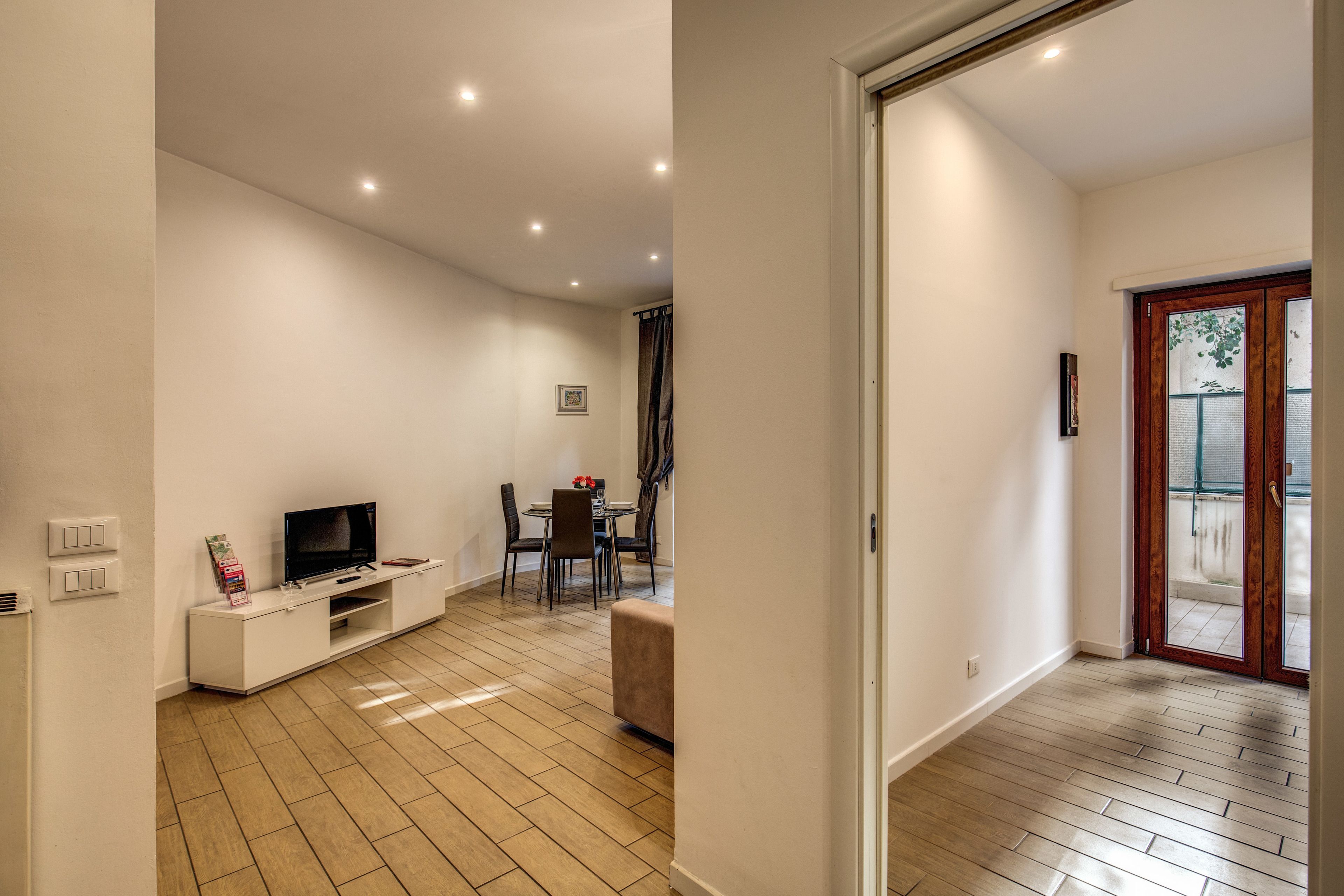 A modern living room with a flat-screen TV, a dining area with a table and chairs, and a wooden floor.