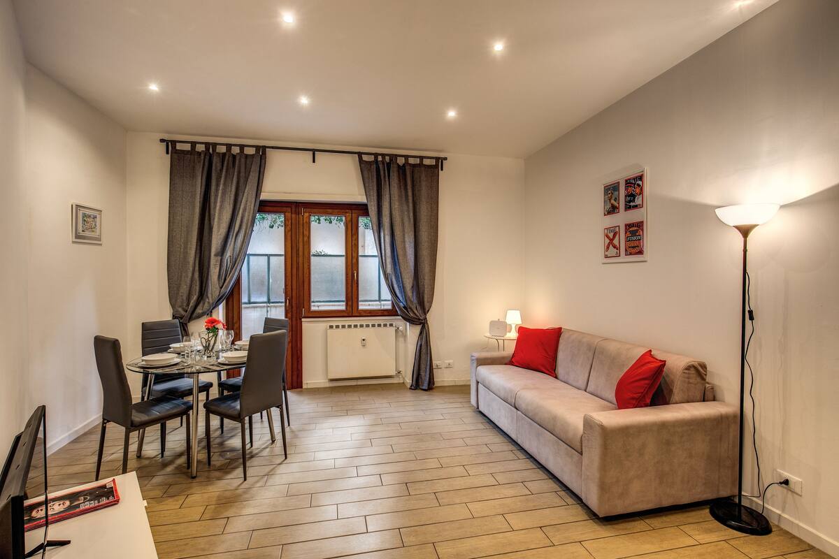 A living room with a sofa, a dining table with chairs, a radiator, and a floor lamp.