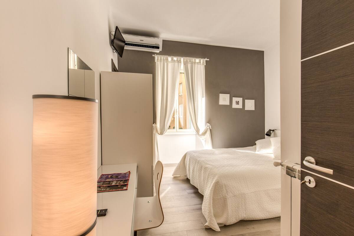 A bedroom with a bed, a desk, a chair, a wardrobe, and a window with curtains.