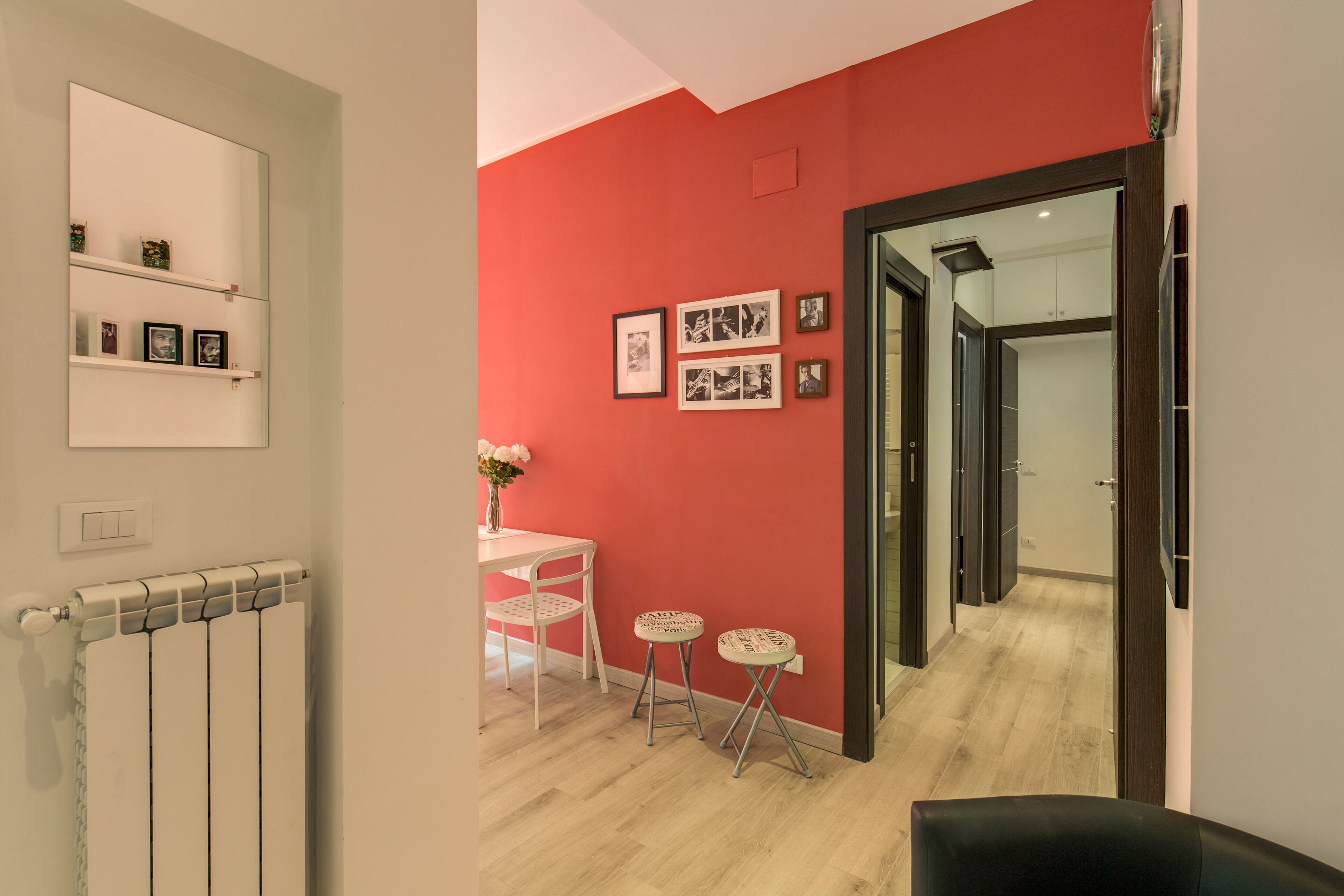 A modern interior with a red accent wall, a white radiator, a small table with a vase, and two stools.