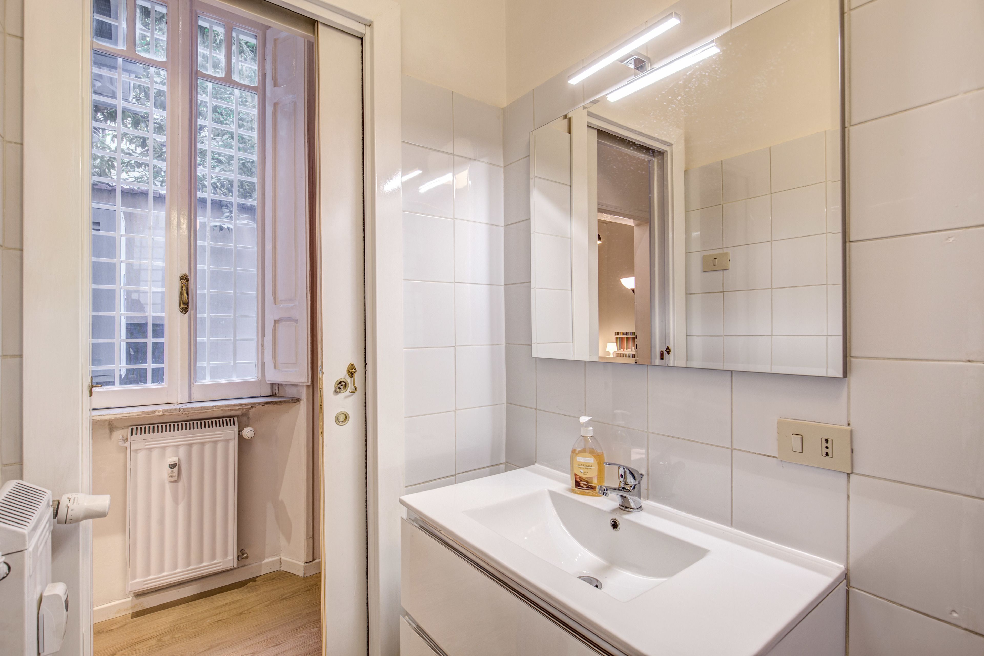 A bathroom with a white sink, mirror, and window.