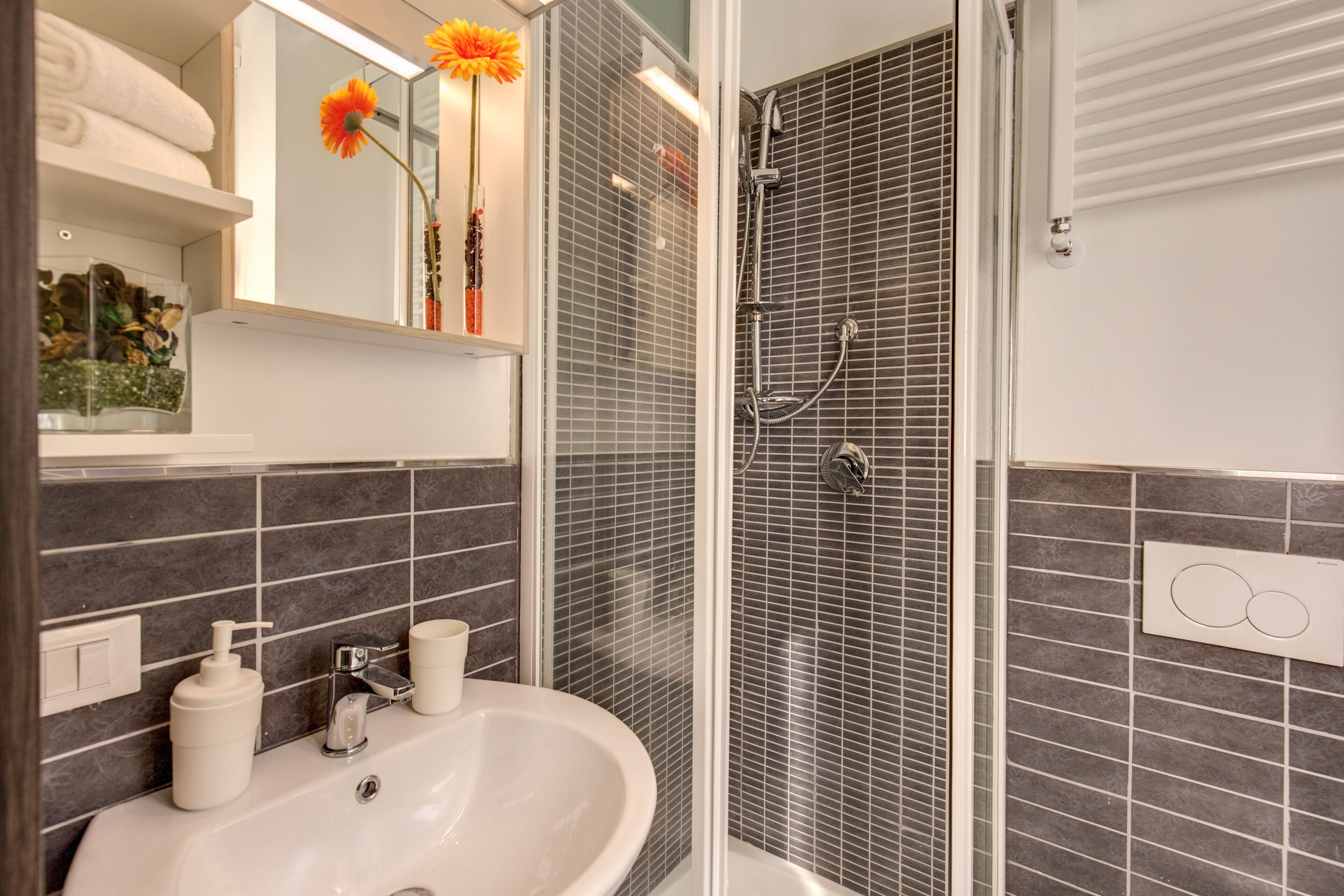 Een badkamer met een wastafel, spiegel, douche en handdoekhouder.