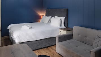 A bedroom with a bed, a grey sofa, a wooden table, and a nightstand.