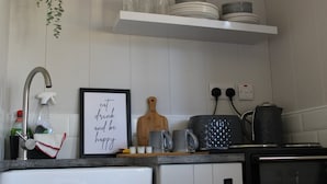 Een keuken met een spoelbak, kraan en een lijst met de tekst 'eat drink and be happy'. Boven een plank met borden en een snijplank op het aanrecht.