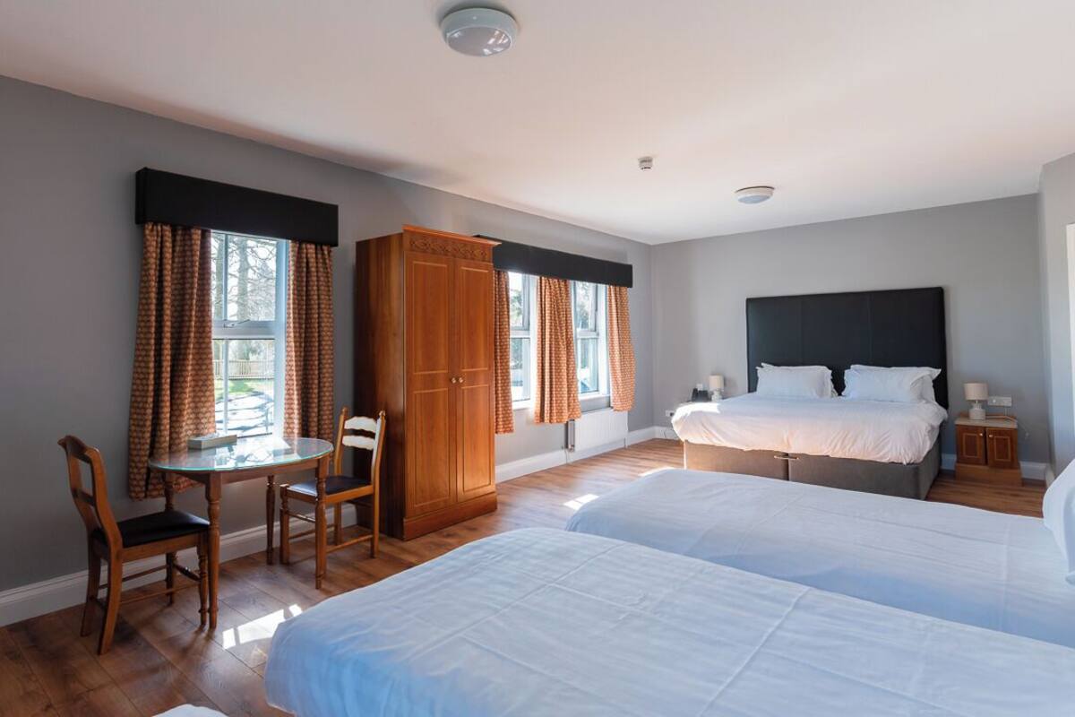 A bedroom with two beds, a wooden wardrobe, a dining table with chairs, and a window with curtains.