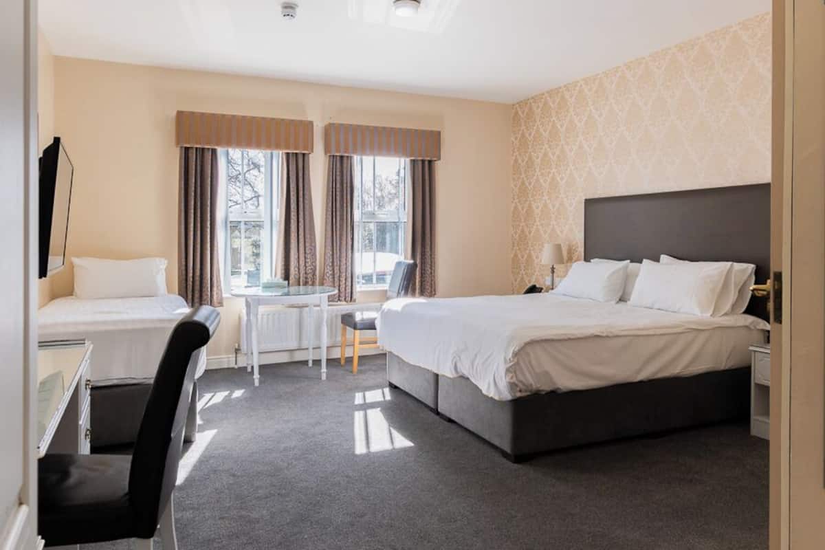 A hotel room with a bed, desk, chair, and a view of the outdoors.