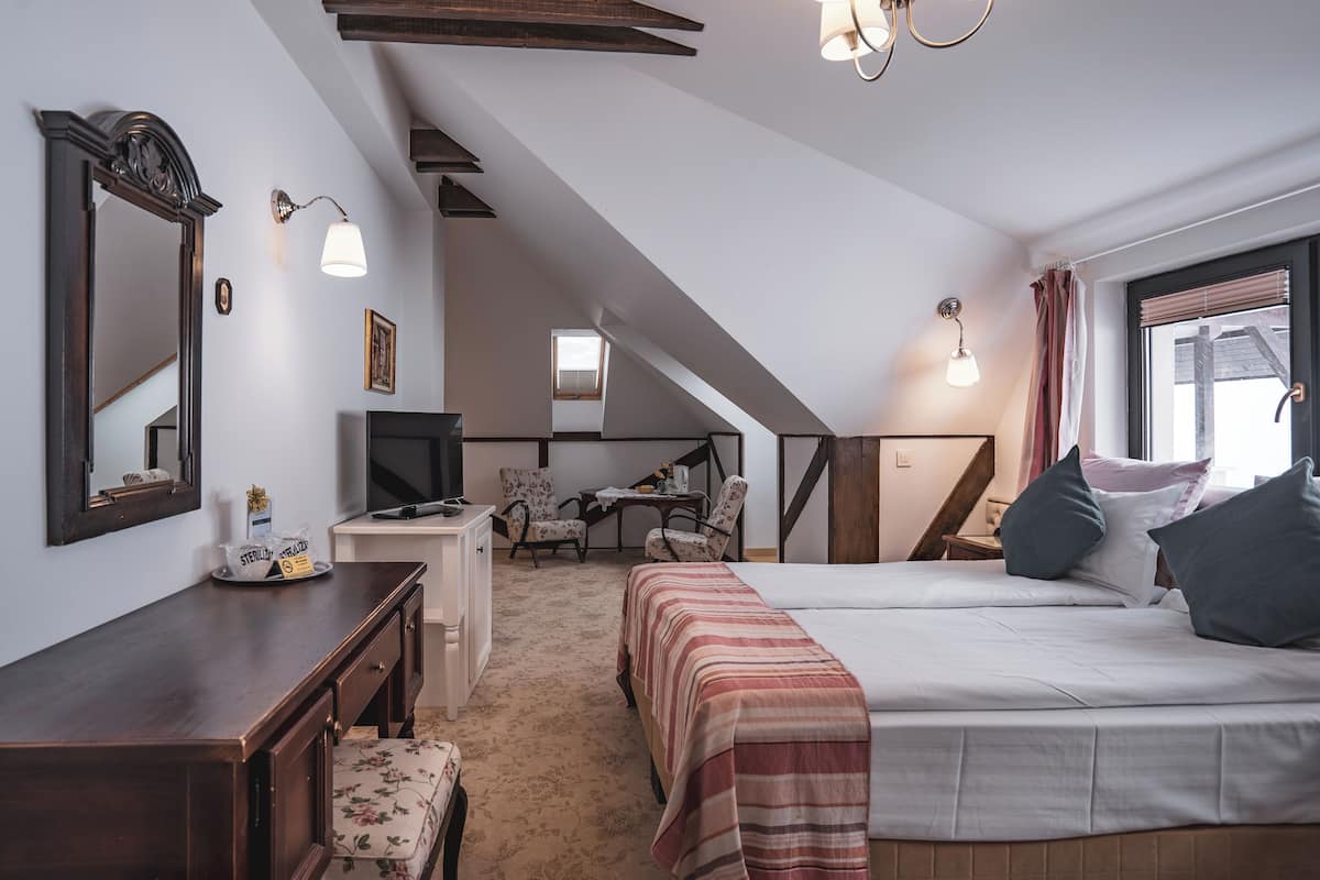 Quarto com duas camas, uma escrivaninha, uma cadeira, uma televisão e uma janela com cortinas.
