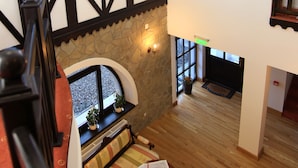 Un interior espacioso con techo alto, una araña de cristal, chimenea y ventanas amplias.