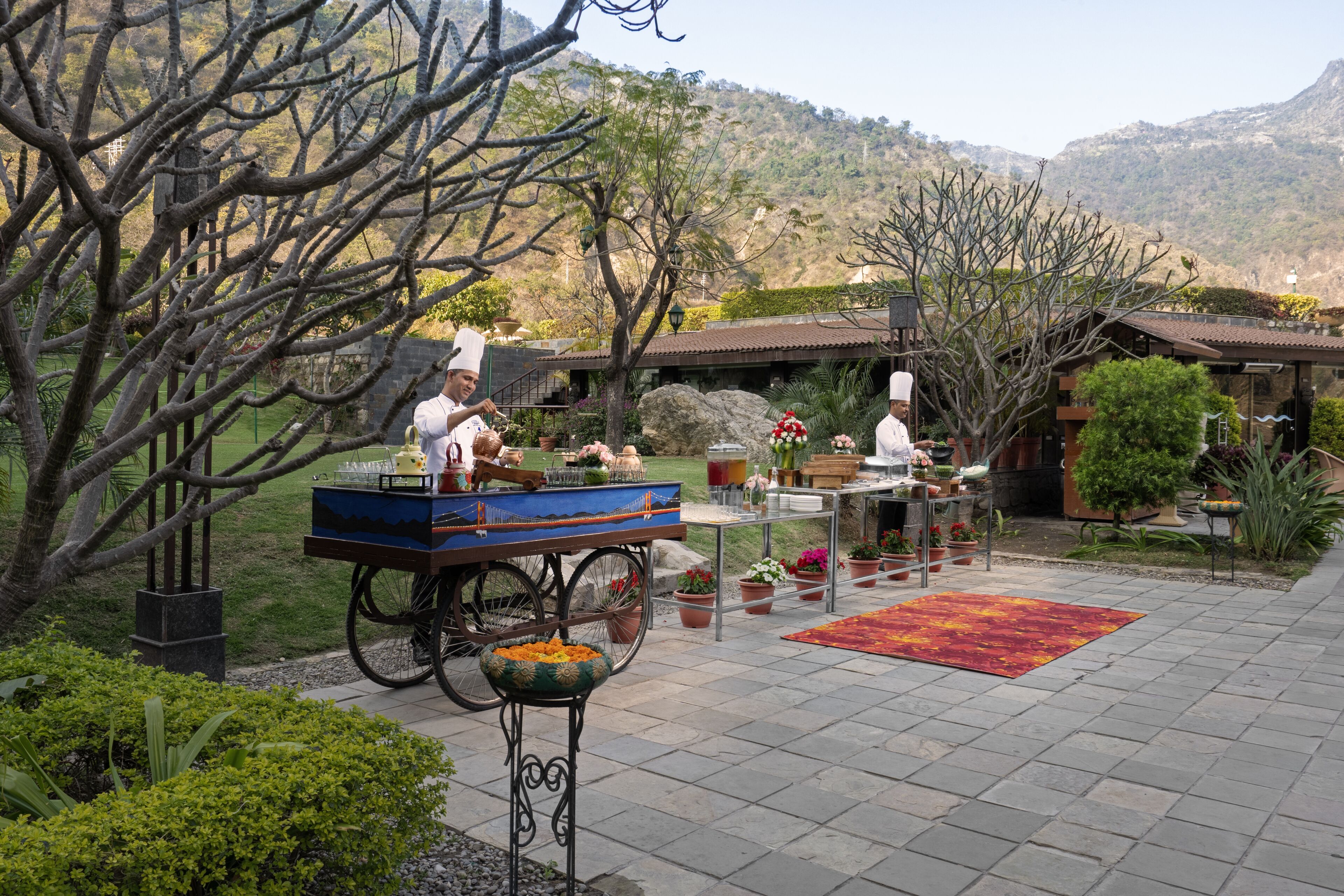 Un patio con un carrito de comida, una mesa de comedor con sillas y montañas al fondo.