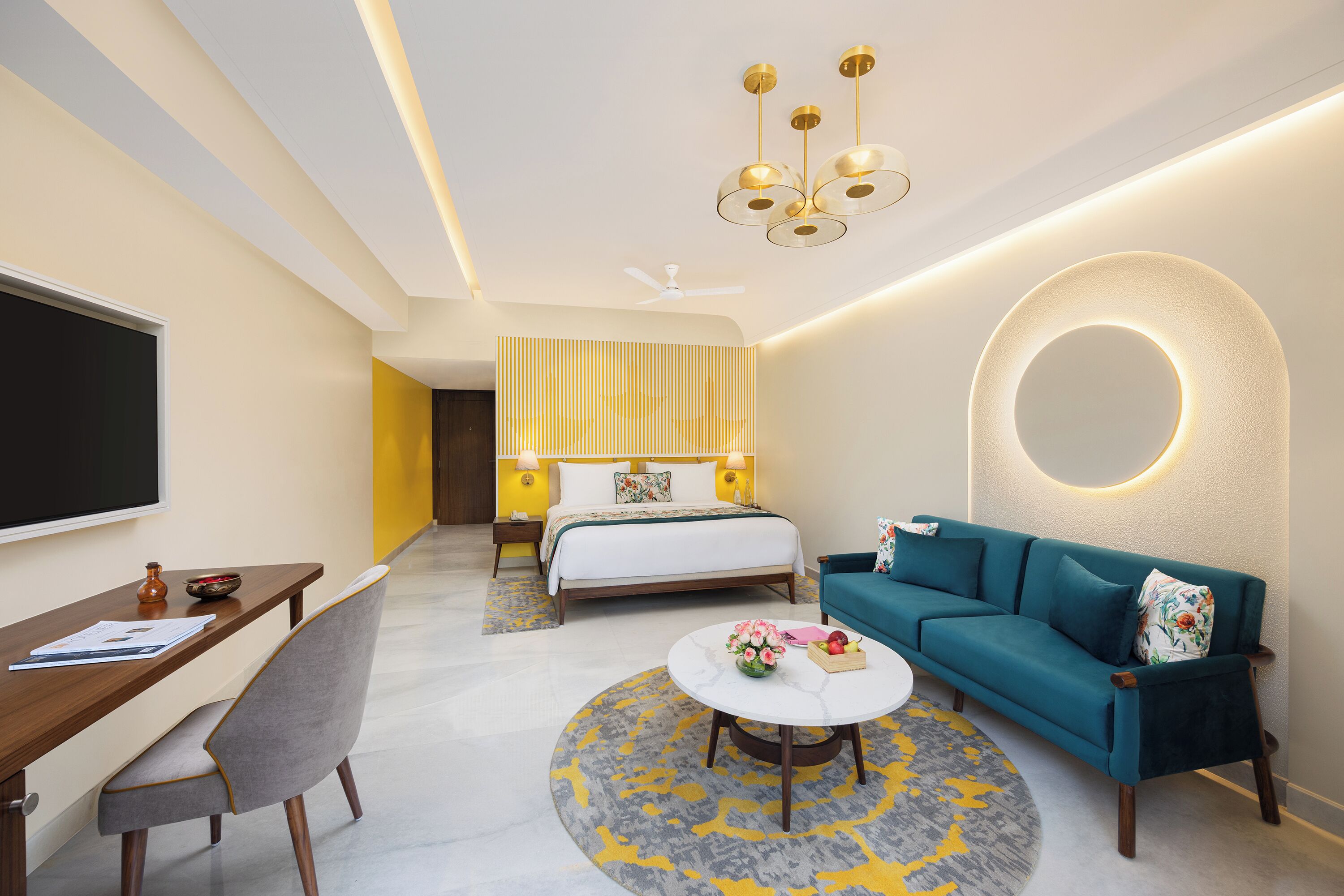 A modern hotel room with a bed, a sofa, a desk, and a round coffee table.