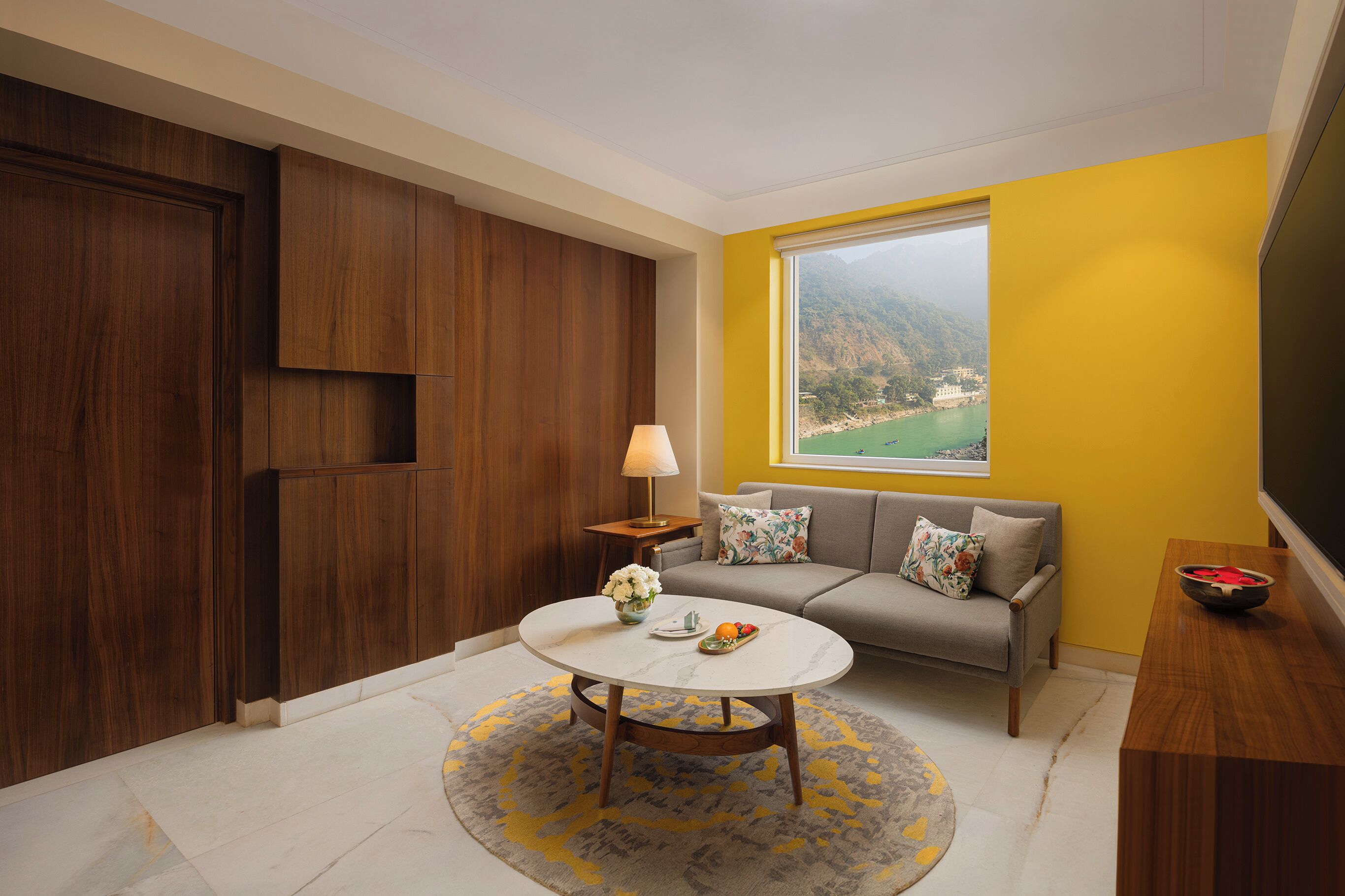 A modern living room with a sofa, a coffee table, and a view of a mountainous landscape through a large window.