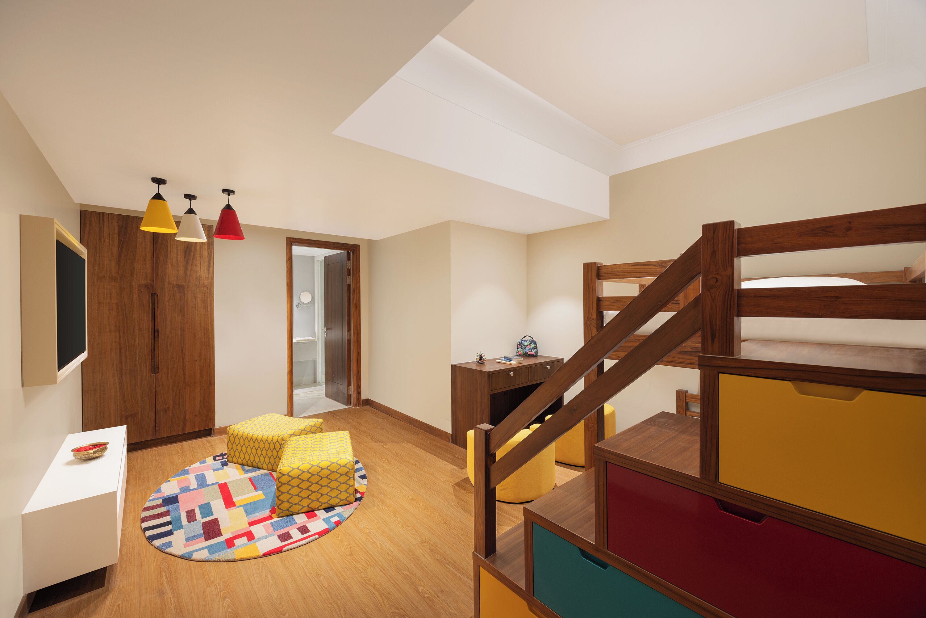 A room with a bunk bed, a desk, a chair, a small table, and a colorful rug.