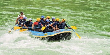 Un grupo de personas en una balsa azul con remos amarillos, navegando por aguas verdes.