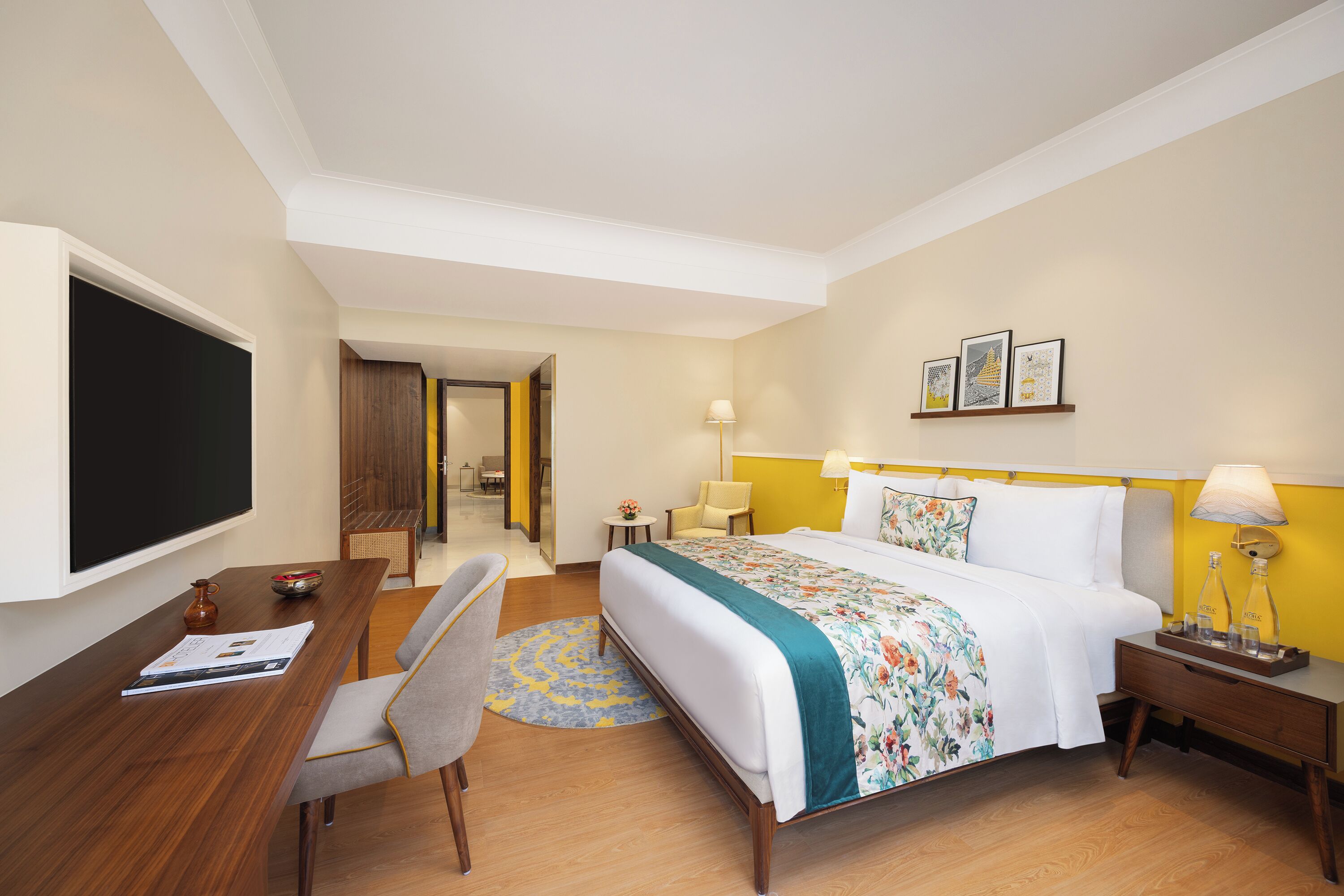 Ein Hotelzimmer mit einem großen Bett, einem Schreibtisch mit Stuhl, einem Flachbildfernseher und einem kleinen Tisch mit Lampe.
