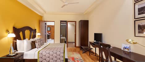 Habitación de hotel con cama, escritorio, silla, televisor y cuadros en la pared.