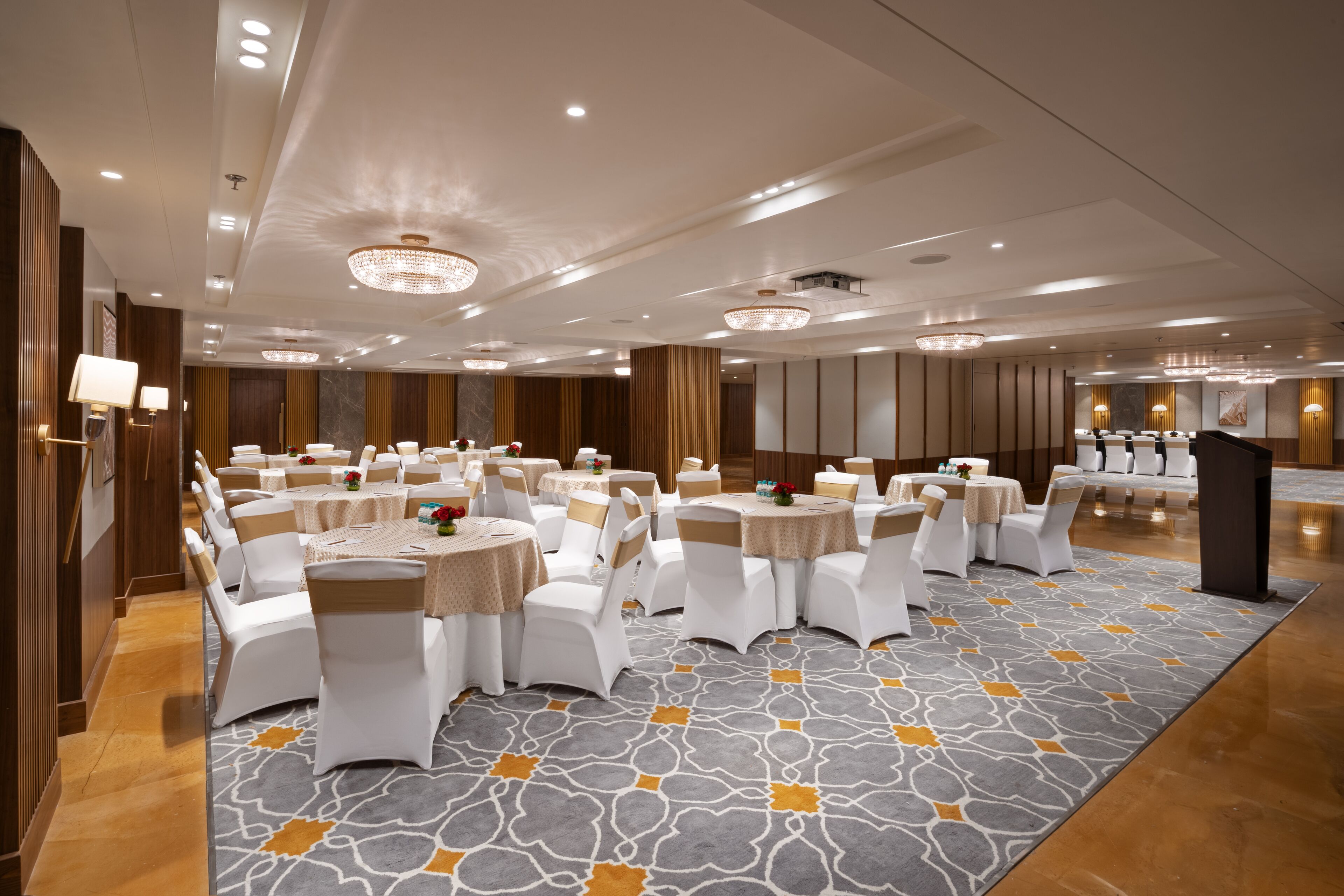 A banquet hall with round tables, white chairs, and a patterned carpet.