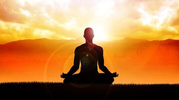 Silueta de una persona meditando con un atardecer de fondo.