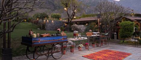 Une terrasse avec un chariot, une table et des chaises, entourée de plantes en pot et offrant une vue sur les montagnes.