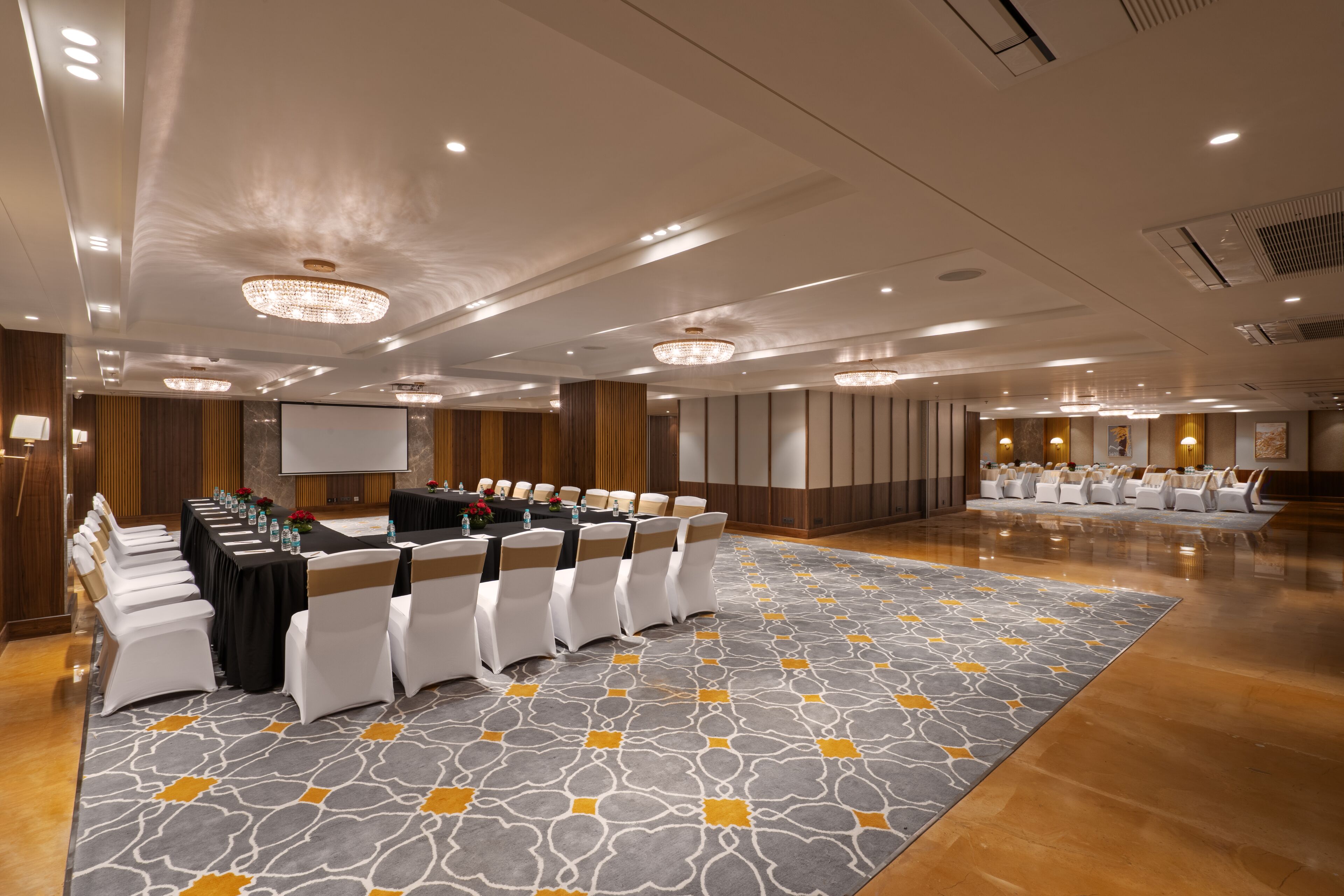 A conference room with a long table, white chairs, and a patterned carpet.