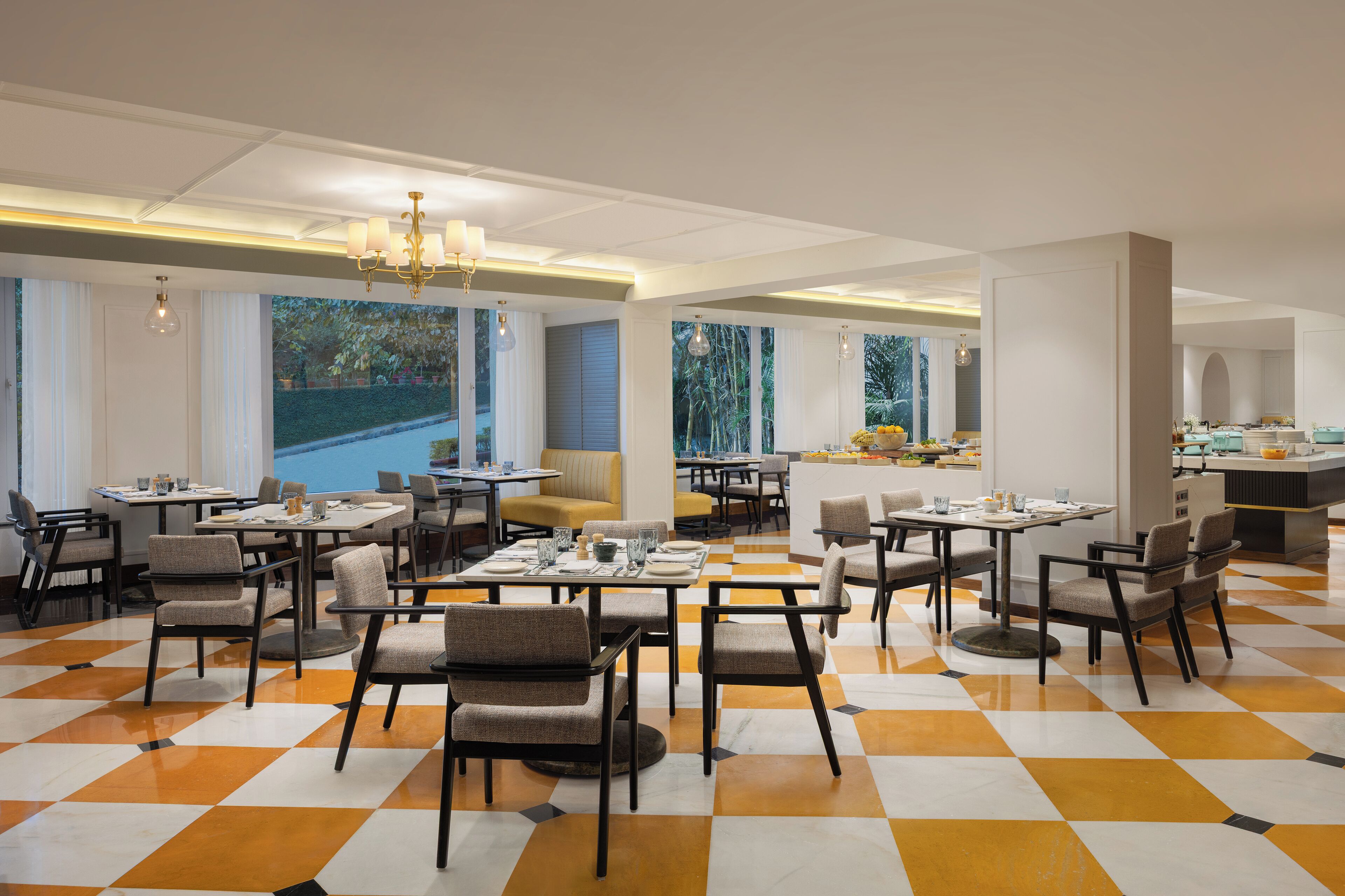 A spacious dining area with multiple tables and chairs, large windows offering a view of greenery, and a checkered floor pattern.