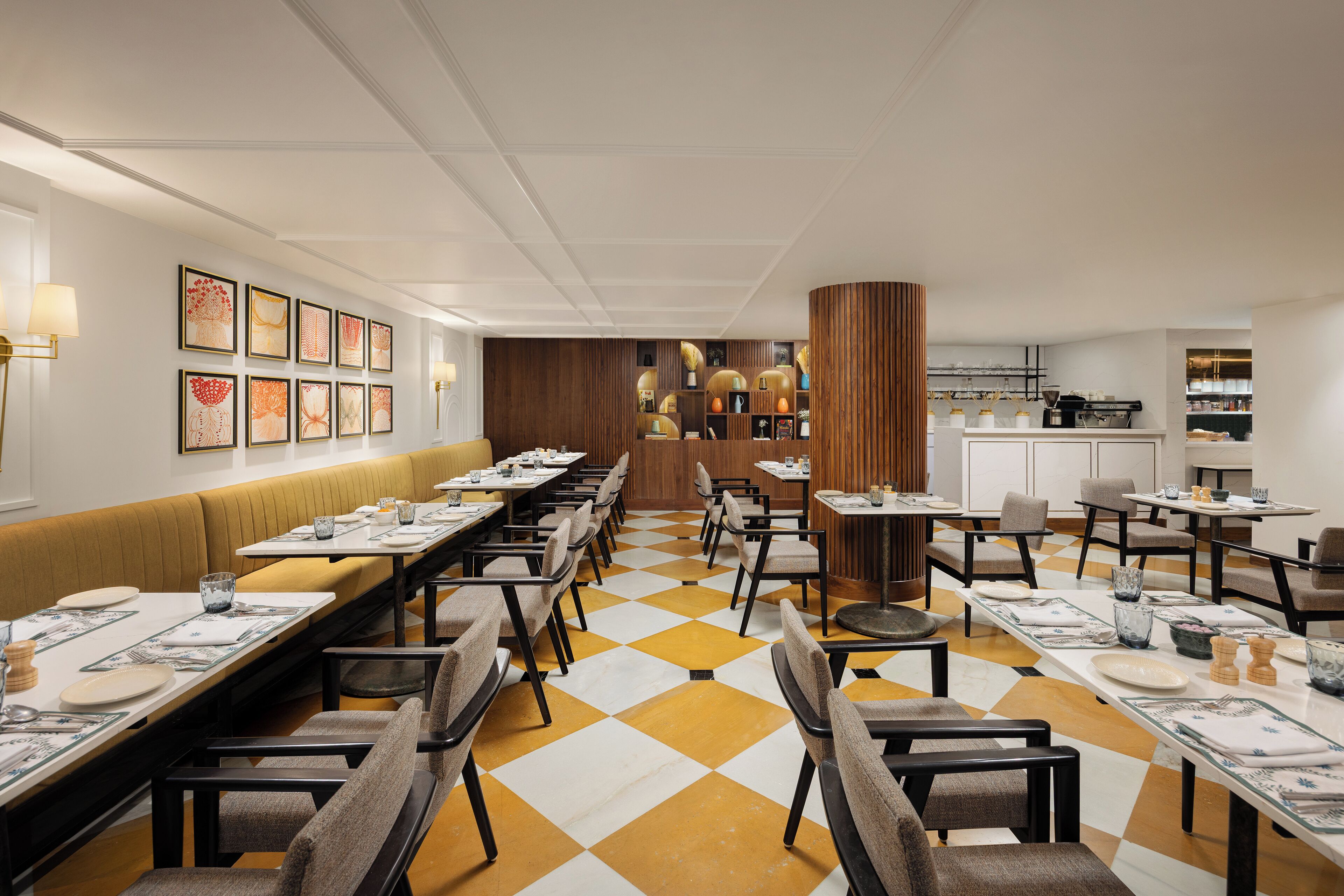 A restaurant with a checkered floor, long tables, and booths. There are framed pictures on the wall and a kitchen area in the background.